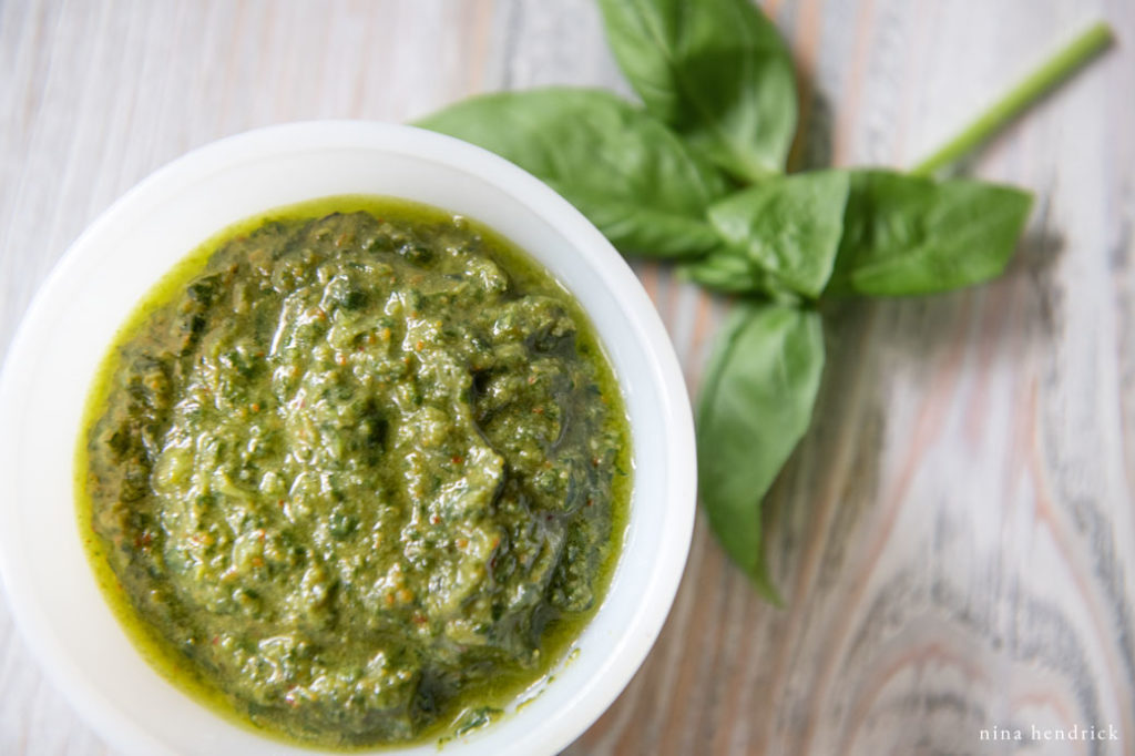 a white bowl of green basic basil pesto with basil leaves